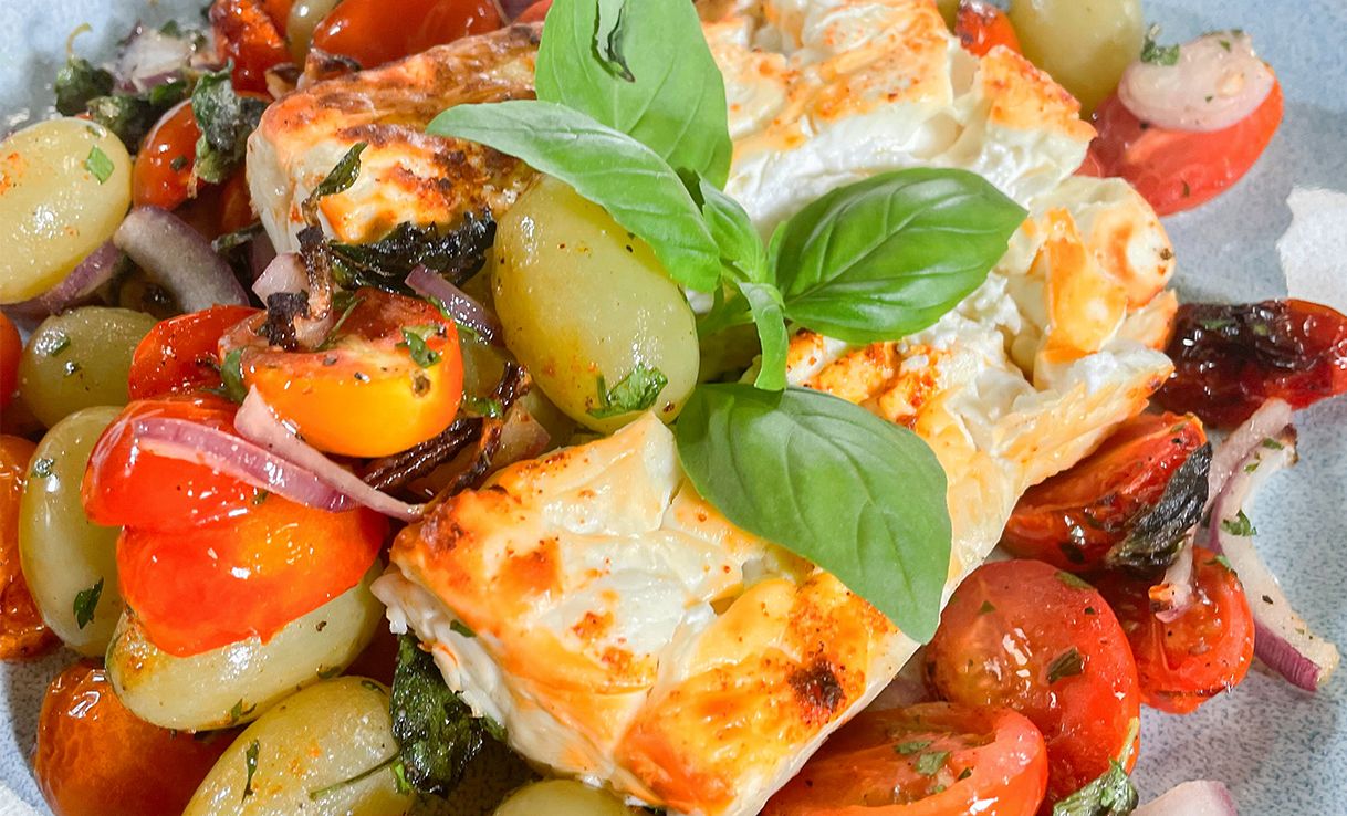 Ofenfeta mit Cherrytomaten, Trauben und einem Basilikumblatt als Garnitur