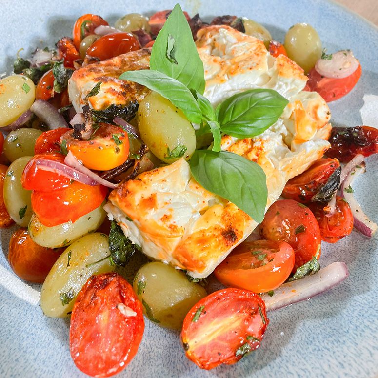 Ofenfeta mit Cherrytomaten, Trauben und einem Basilikumblatt als Garnitur
